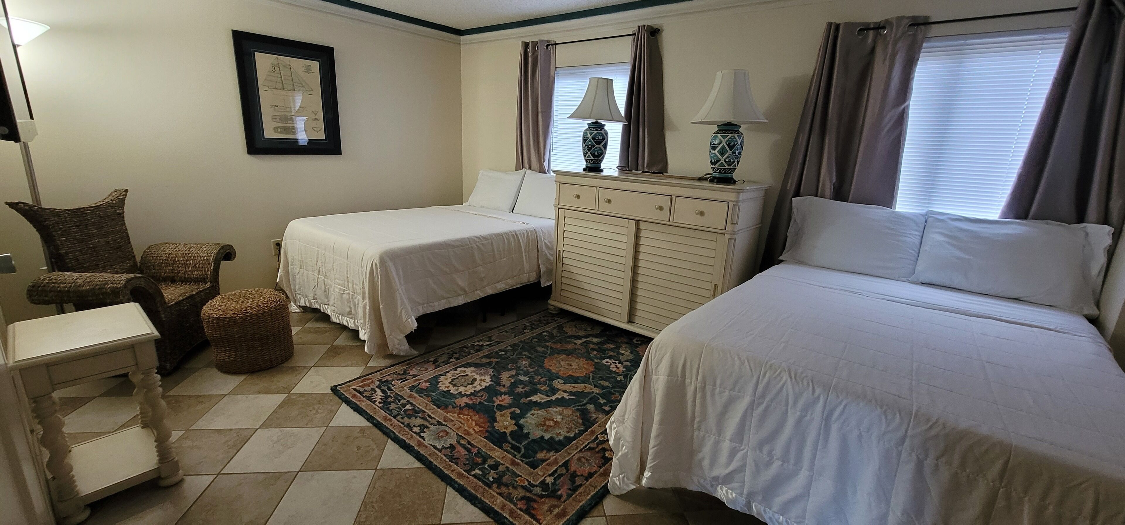 Une chambre d’hôtel avec deux lits, une petite table, une chaise, une commode et un tapis décoratif.