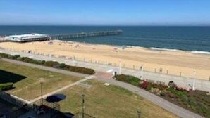 Vista de una playa con un muelle que se adentra en el agua, arena y un camino que lleva a la playa.