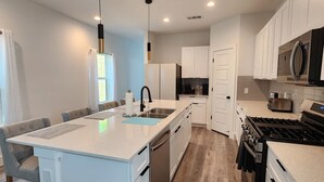 A modern kitchen with white cabinetry, a central island, stainless steel appliances, and a wooden floor. - Dallas Home (Dallas)