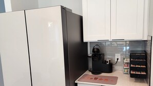 A compact kitchen with white cabinets, a black refrigerator, a coffee maker, and a spice rack. - Dallas Home (Dallas)