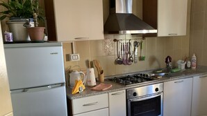 Une cuisine compacte équipée d’un réfrigérateur, d’une cuisinière, d’un four et de placards. On y trouve des plantes en pot sur le plan de travail et une petite table recouverte d’une nappe.