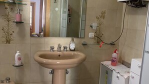 Une salle de bain avec un lavabo beige, un miroir et un espace douche. On y trouve des articles de toilette rangés sur des étagères et dans un meuble.