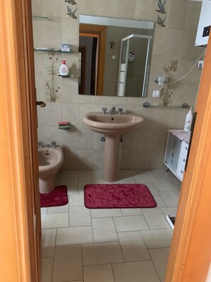 A bathroom with a sink, bidet, and mirror. There are decorative tiles on the walls and a red bath mat on the floor.