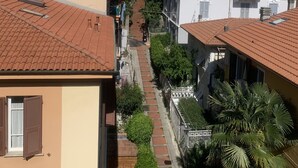 Une rue étroite bordée d’immeubles à plusieurs étages dotés de balcons, un ciel dégagé et un trottoir pour les piétons.