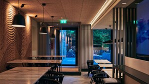 En modern restaurang med träbord och stolar, hängande lampor och utsikt över gatan utanför.