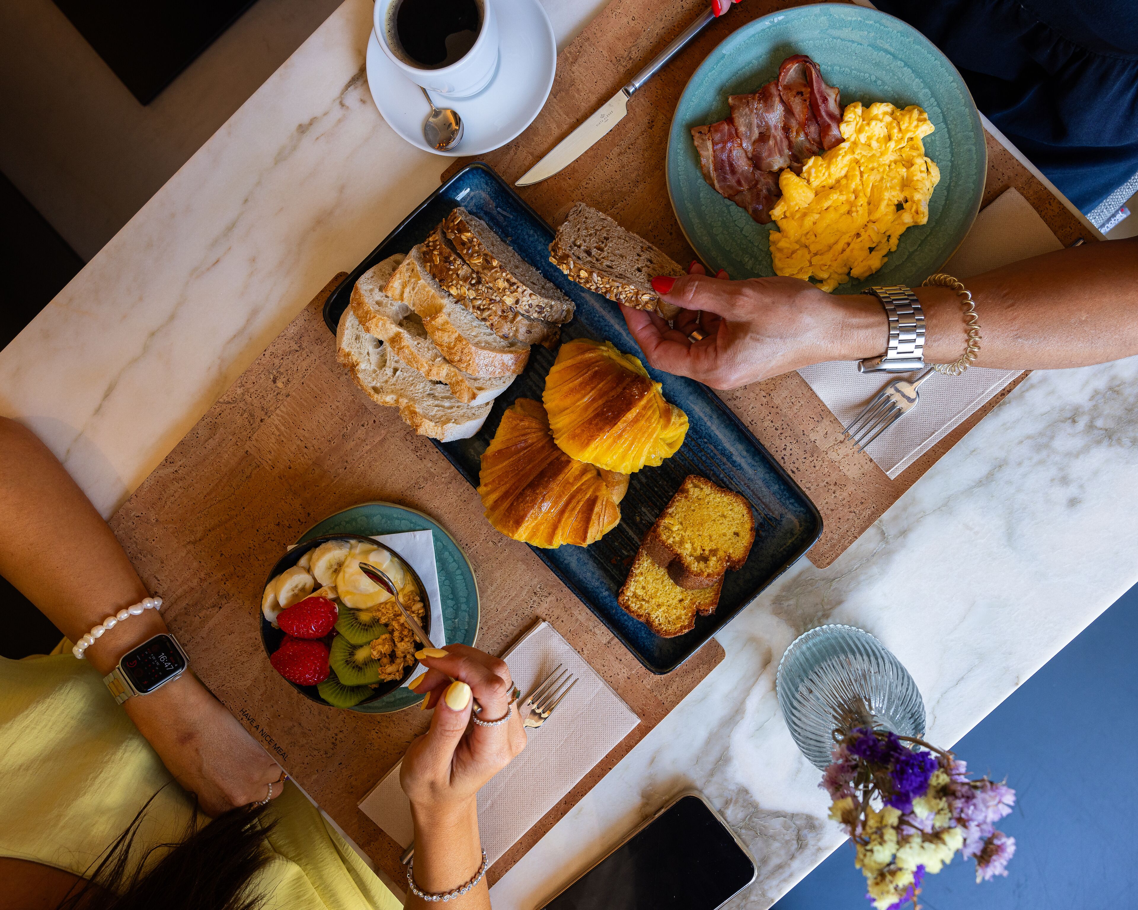 Una mesa de desayuno con diferentes alimentos, una taza de café y un teléfono inteligente.