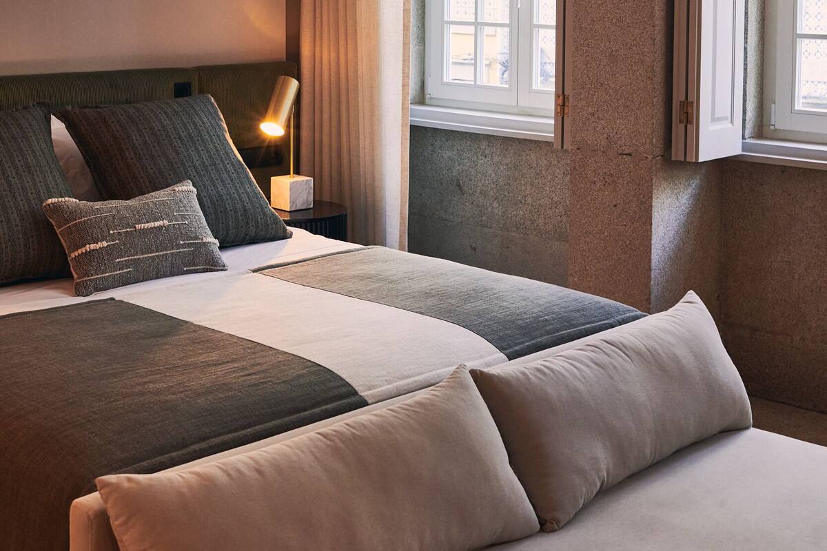 Una habitación de hotel con una cama grande, una mesita de noche con lámpara y una ventana con cortinas.