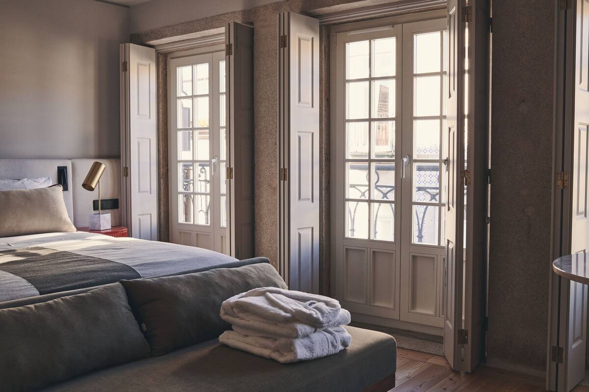 Un dormitorio con cama, una mesita de noche, una lámpara y vistas al balcón exterior por una puerta.