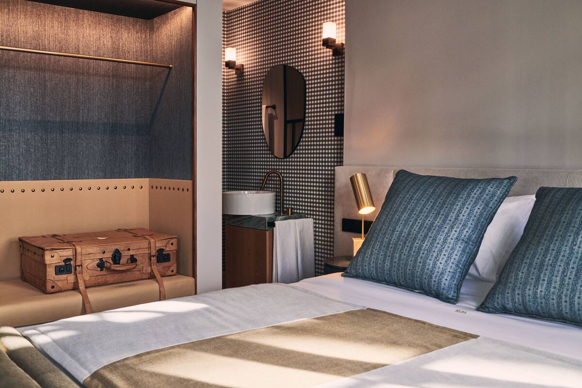 Habitación de hotel con cama, maleta, espejo y pared con diseño a cuadros.