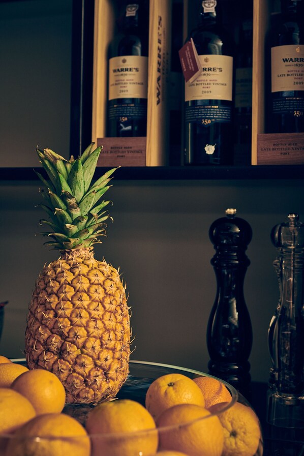 Un ananas sur une table, avec des oranges, et des bouteilles en arrière-plan.