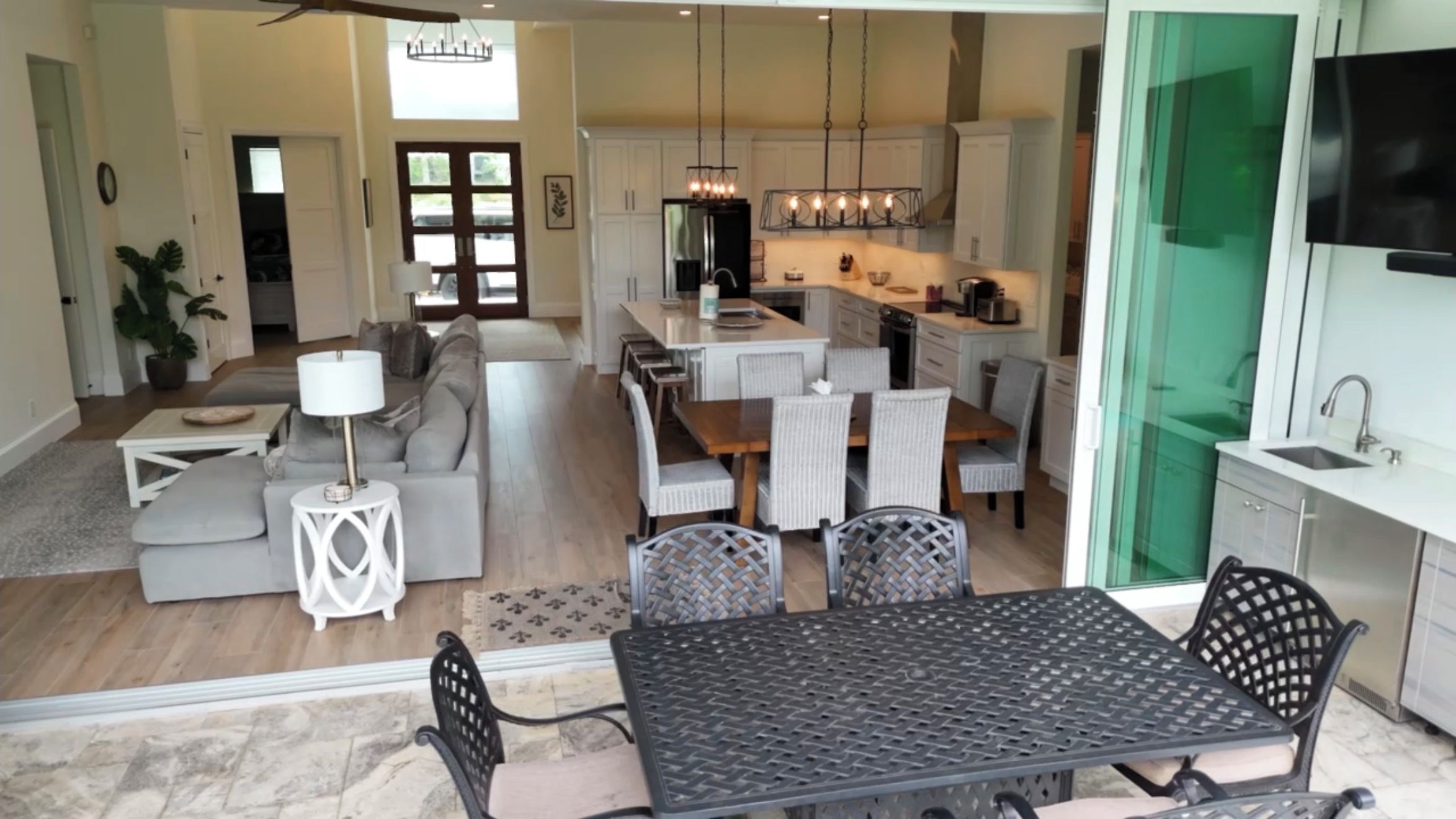 A modern kitchen with white cabinets, a central island, and a dining area with a black metal table and wicker chairs.
