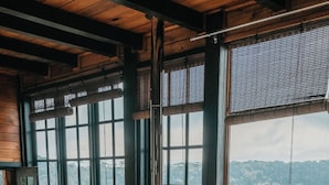 Una habitación acogedora con ventanas amplias, una estufa de leña, una silla de madera y un taburete pequeño.