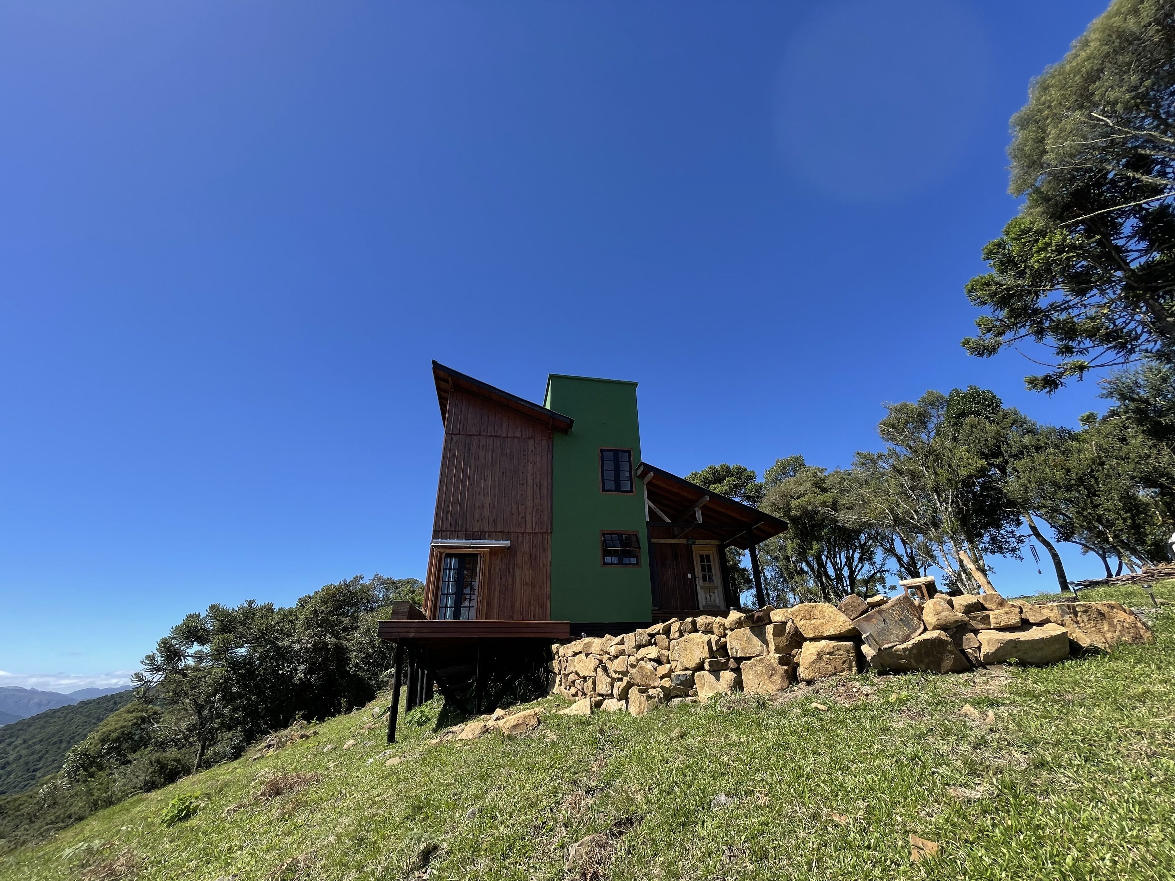 Una casa moderna con un techo inclinado peculiar, ubicada en una ladera cubierta de césped y con base de piedra.