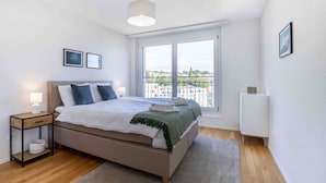 A bedroom with a bed, bedside tables, a window with a view, and a radiator. - Arsenaux Residence by Homenhancement (Fribourg)