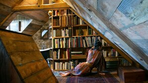 A cozy attic room with a wooden sloped ceiling, a large bookshelf filled with books, and a patterned rug on the floor. - Les Maisons du Bonheur & Balnéo (Croze)