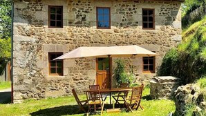 A stone house with a red-tiled roof, a wooden door, and a patio with a table and chairs. - Les Maisons du Bonheur & Balnéo (Croze)
