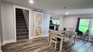 A dining area with a wooden table and chairs, a kitchen in the background, and a staircase with a wooden door. - Beautiful Country Setting Welcome to Moberly Manor (Depauw)