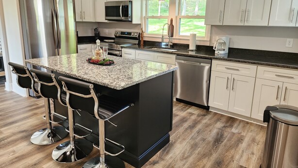 A modern kitchen with white cabinets, stainless steel appliances, a granite countertop, and a bar area with stools. - Beautiful Country Setting Welcome to Moberly Manor (Depauw)