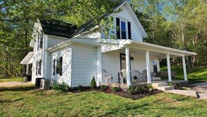 A white two-story house with a covered porch, a small garden, and a clear blue sky. - Beautiful Country Setting Welcome to Moberly Manor (Depauw)