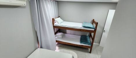 Quarto pequeno e compacto com uma cama beliche, mesa de cabeceira e cortina.