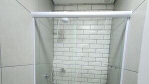 Uma casa de banho pequena e moderna, com sanita, chuveiro com porta de vidro e paredes em azulejo.