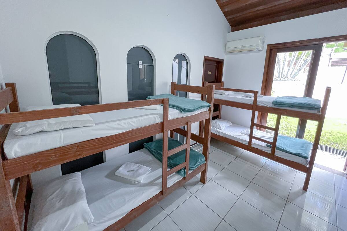 A dormitory room with bunk beds, a window, and an air conditioning unit.