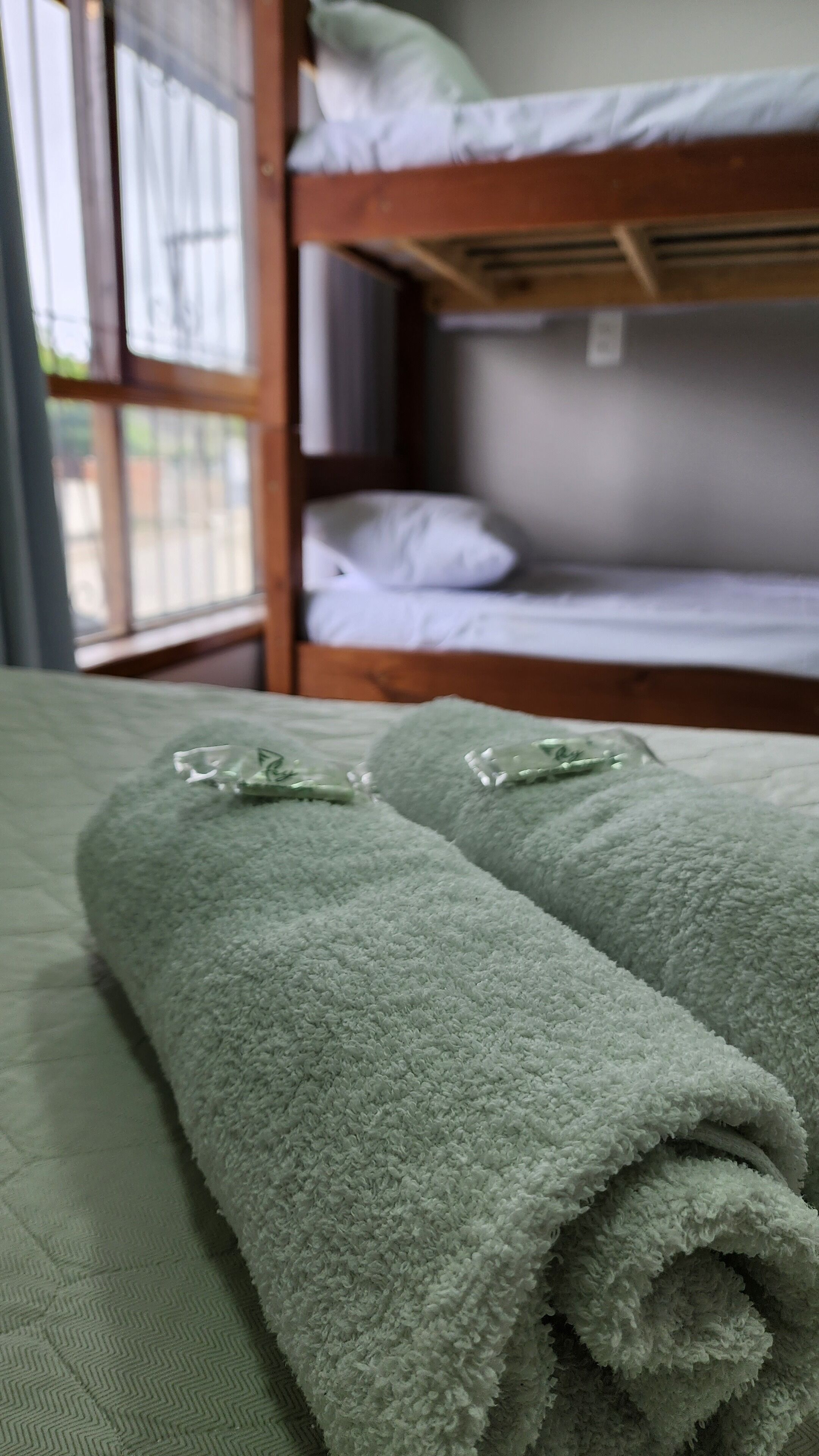 A room with a bunk bed, a green bedspread, and two rolled-up towels on the lower bunk.