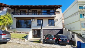 Um edifício de dois andares com varanda, garagem e entrada com carros estacionados.