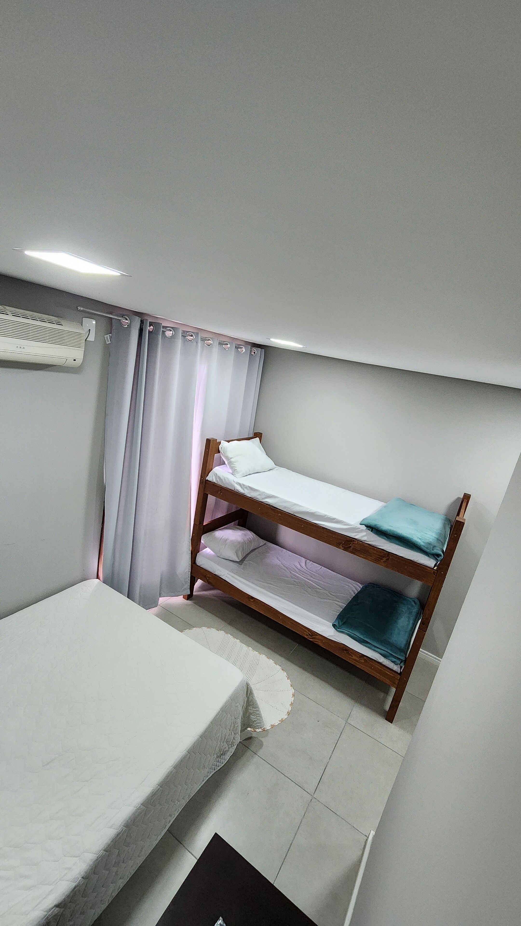 Een eenpersoonskamer met een houten stapelbed, een wit matras en een klein nachtkastje.