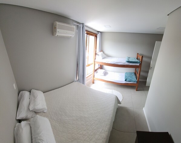 A room with a single bed, a bunk bed in the background, a window with curtains, and a ceiling vent.