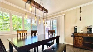 A dining area with a wooden table and benches, a hanging light fixture, and a kitchen area with a coffee maker. - Carlsbad Beach Oasis+HotTub (Carlsbad)