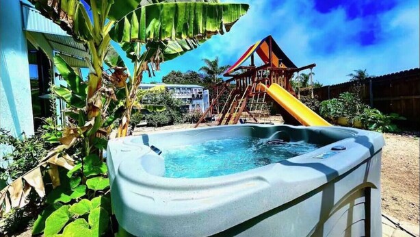 A hot tub in a backyard with a slide and a wooden structure in the background. - Carlsbad Beach Oasis+HotTub (Carlsbad)