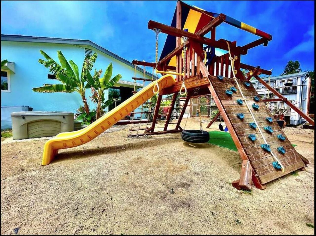 Un'area giochi con scivolo e parete di arrampicata, sullo sfondo di un edificio residenziale.