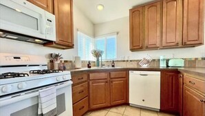 A kitchen with wooden cabinets, a white stove, a microwave, and a dishwasher. - Ocean View Home w/PrivateBalcony (Carlsbad)