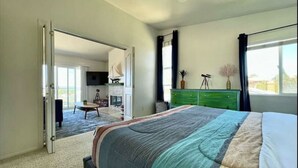 A bedroom with a large bed, a green dresser, a desk with a chair, and a view of the outdoors through a window. - Ocean View Home w/PrivateBalcony (Carlsbad)