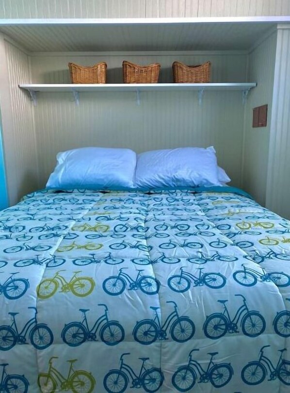 A bed with a bicycle-patterned duvet, a white pillow, and a shelf with three wicker baskets. - Beautiful bungalow three blocks from Lake Michigan (Frankfort)