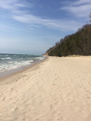 Een strand met een zandrijk strand, golven en een bebost heuvel in de verte.