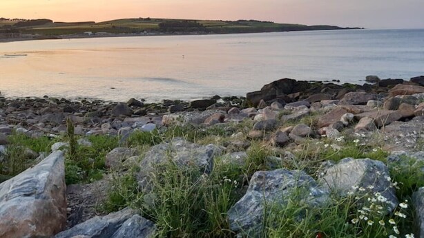 A rocky shoreline with a view of the sea and distant hills.