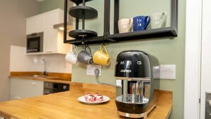 A kitchen with a coffee maker on the counter, a plate of food, and a hanging mug rack above.