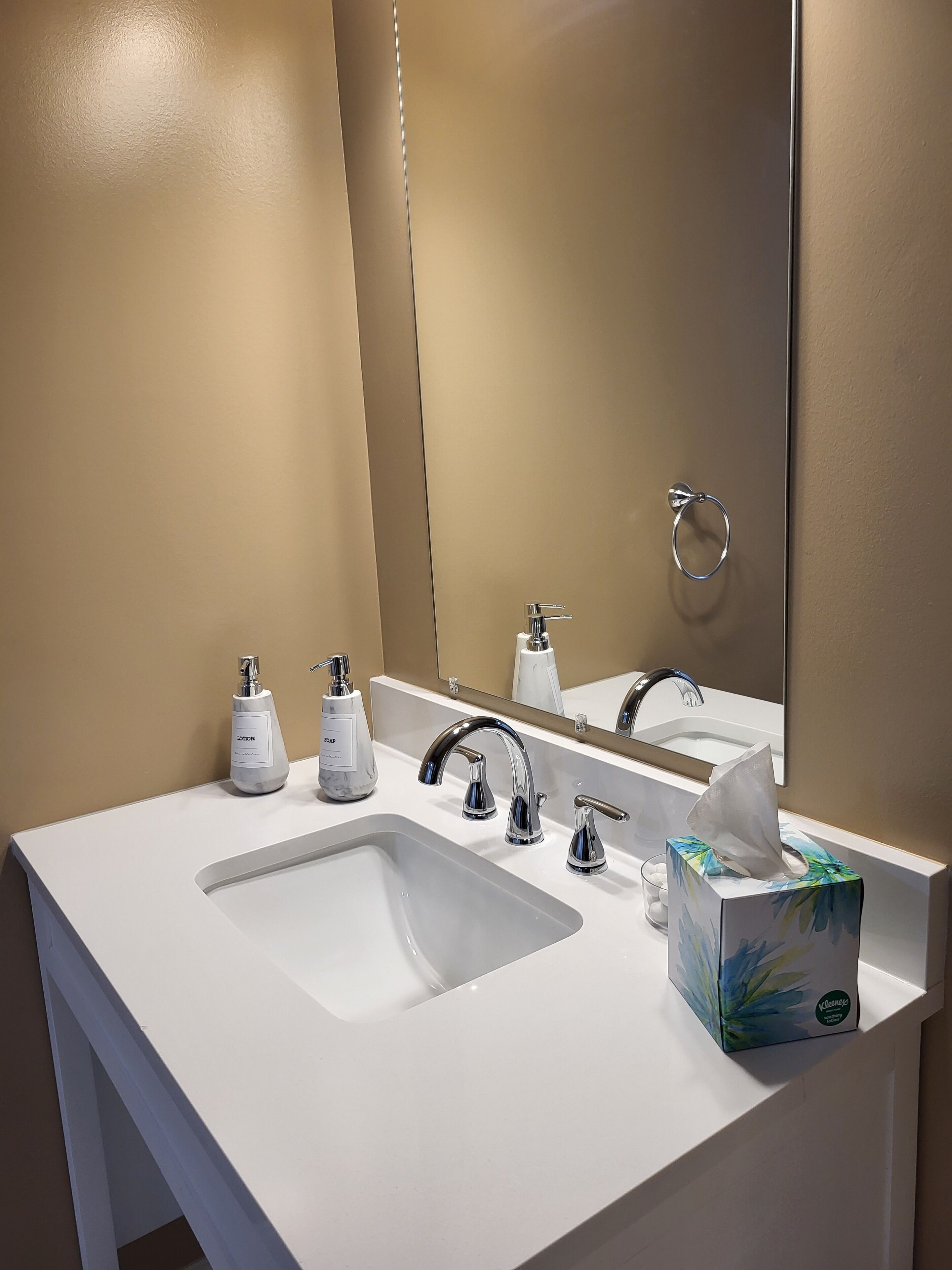 A bathroom with a white sink, two faucets, a mirror, and a tissue box.