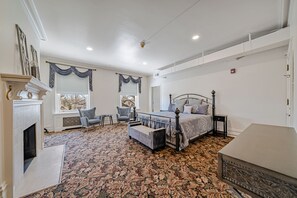 A bedroom with a large bed, a fireplace, a carpeted floor, and a window with curtains. - THE GRANDEUR ESTATE (Greensburg)
