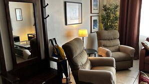 A living room with two armchairs, a sofa, a lamp, a mirror, and a plant. - Condo with pool, walking distance to beach, groceries and several restaurants (Pompano Beach)
