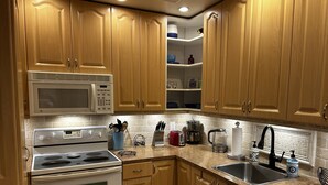 A kitchen with wooden cabinets, a microwave, a stove, a sink, and various kitchen appliances. - Condo with pool, walking distance to beach, groceries and several restaurants (Pompano Beach)
