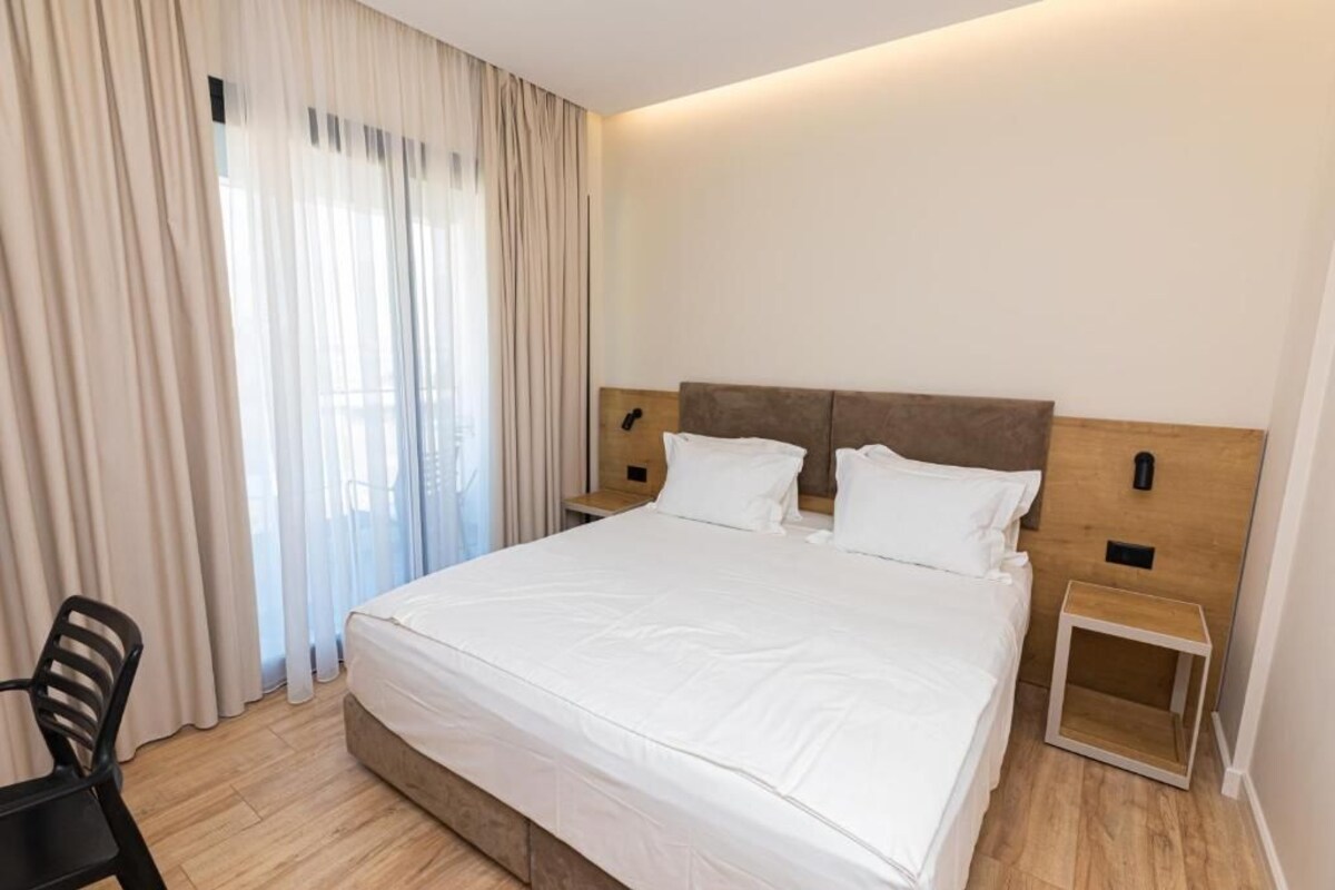 A hotel room with a large bed, a wooden headboard, a bedside table, and a chair.