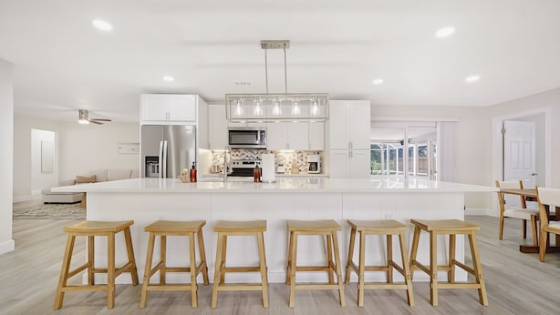 Una cucina moderna con isola centrale, sgabelli da bar, elettrodomestici in acciaio inossidabile e un'ampia finestra.