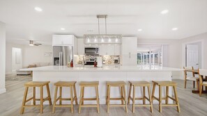 A modern kitchen with a central island, bar stools, stainless steel appliances, and a large window.