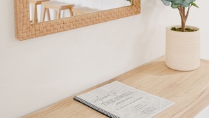 Uno specchio incorniciato appeso al muro, una pianta in vaso e un quaderno su un tavolo di legno.