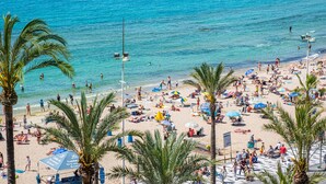 A crowded beach with palm trees, umbrellas, and people enjoying the seaside.