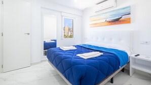 A modern bedroom with a large bed, a painting of a boat on water, and a cityscape view through a window.