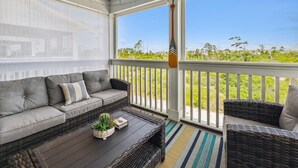 A covered porch with a gray sofa, wicker chairs, a wooden table with plants, and a view of greenery. - NEW LISTING! Lost Key Golf & Beach Club~ Happy Ours -  NO HASSLE CHECK OUT (Pensacola)